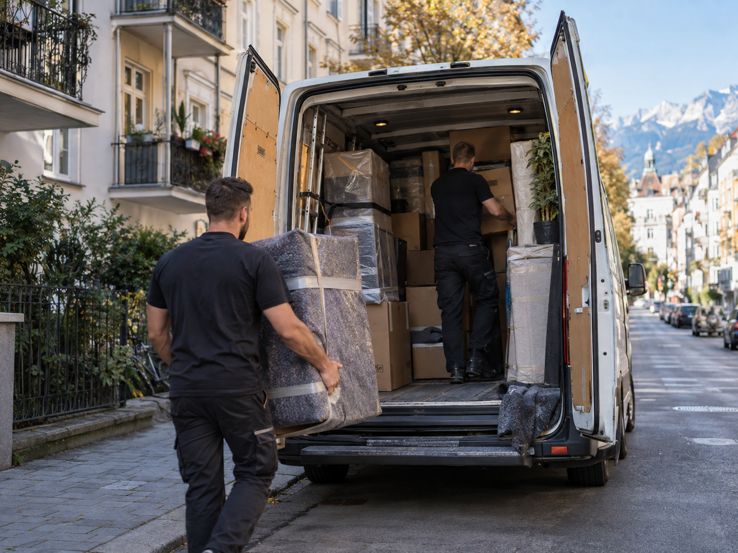 Zwei Umzugshelfer laden verpackte Möbel und Kartons in einen geöffneten weißen Transporter